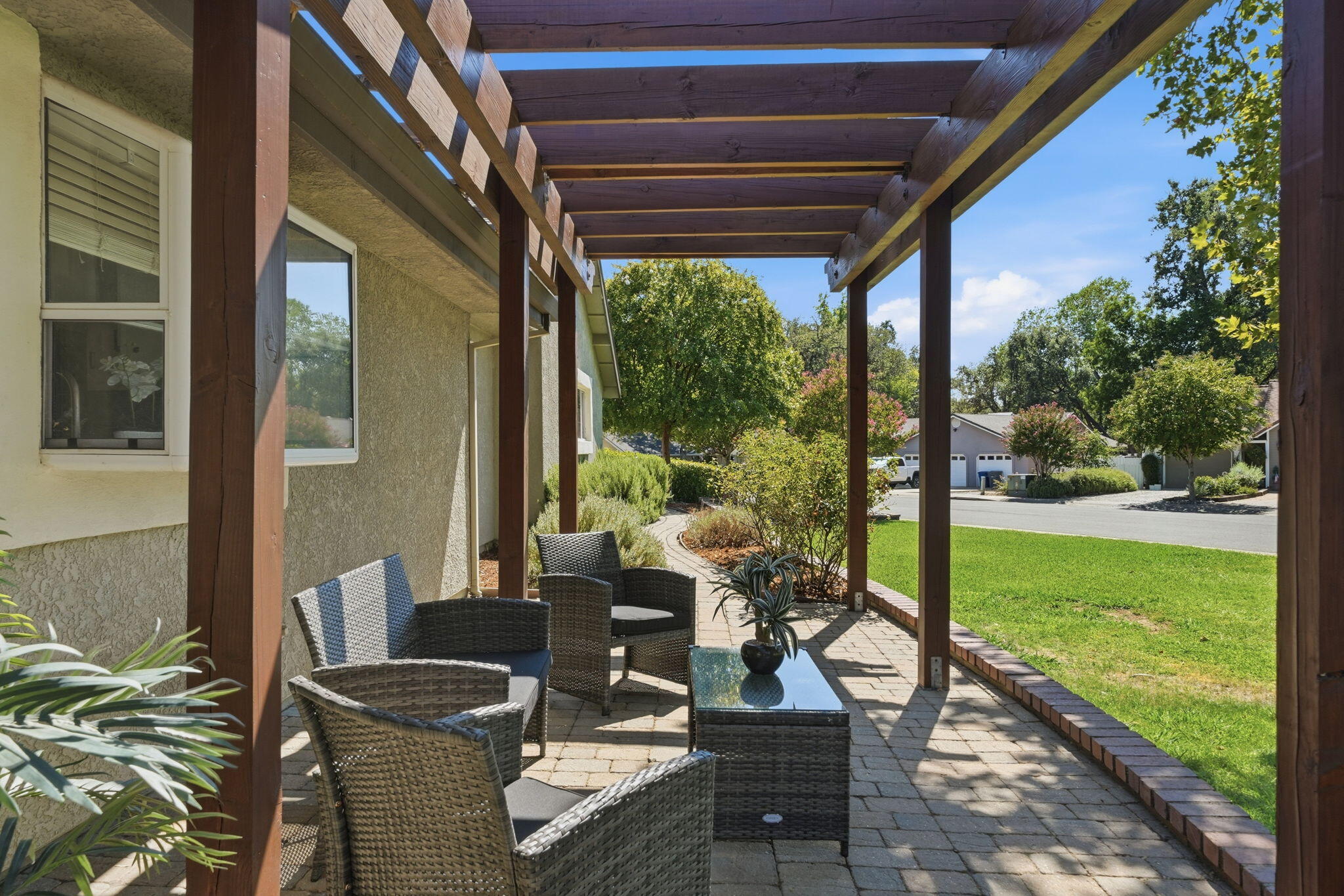Covered patio with a wooden pergola, wicker seating, and views of the lawn and garden.