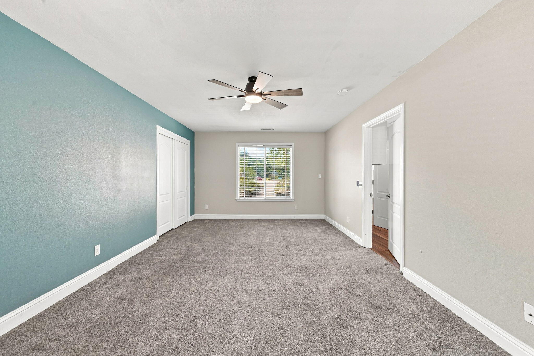 Empty bedroom with gray carpet, a teal accent wall, ceiling fan, and double-door closet.