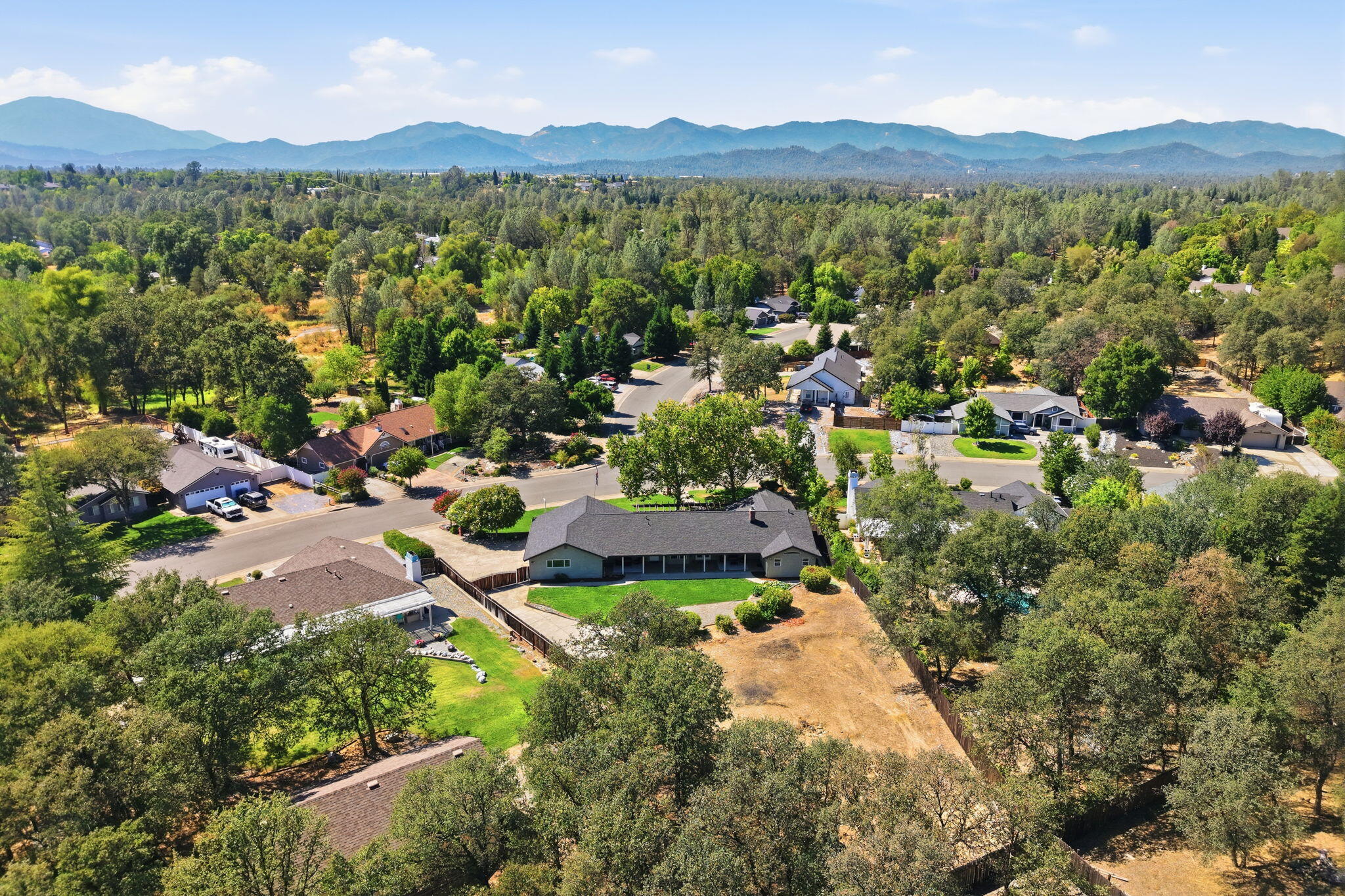 Aerial view of a single-story home with a fenced yard and mountain views.