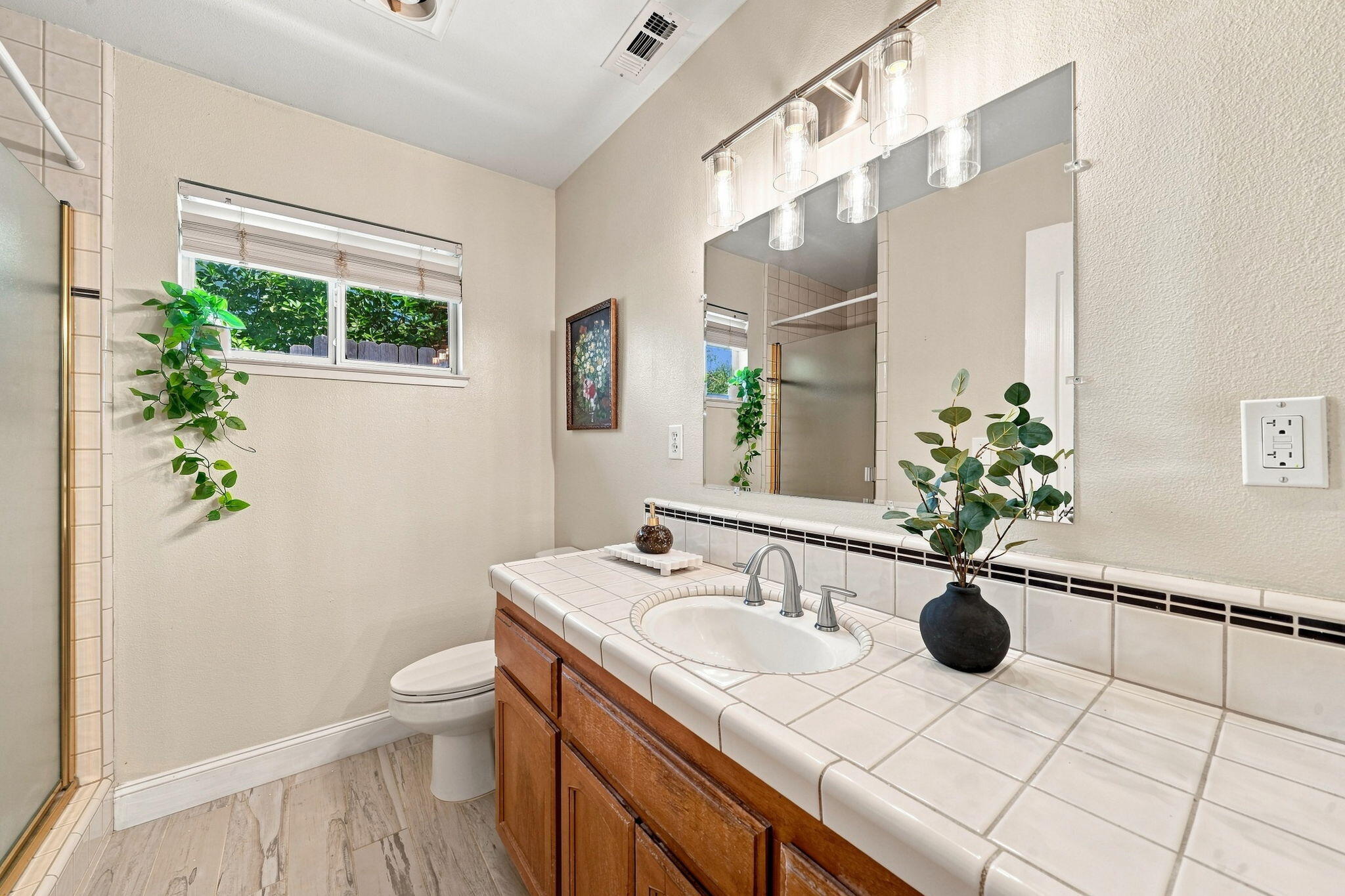 Bathroom with tiled vanity, large mirror, vessel-style lighting, and a window beside the toilet.