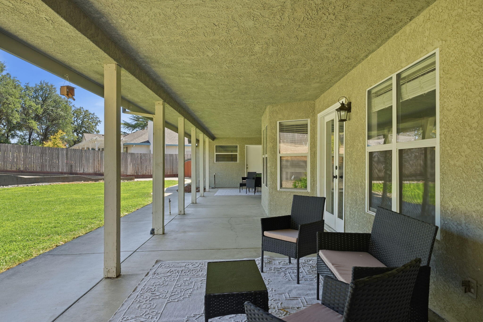 Covered back patio with wicker seating overlooking a fenced lawn.