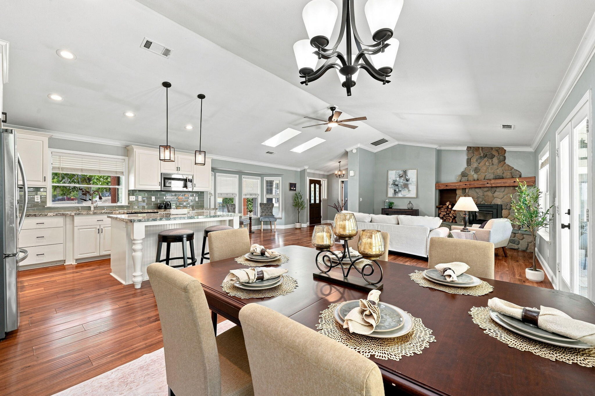 Open-plan kitchen, dining area, and living room with hardwood floors and a stone fireplace.