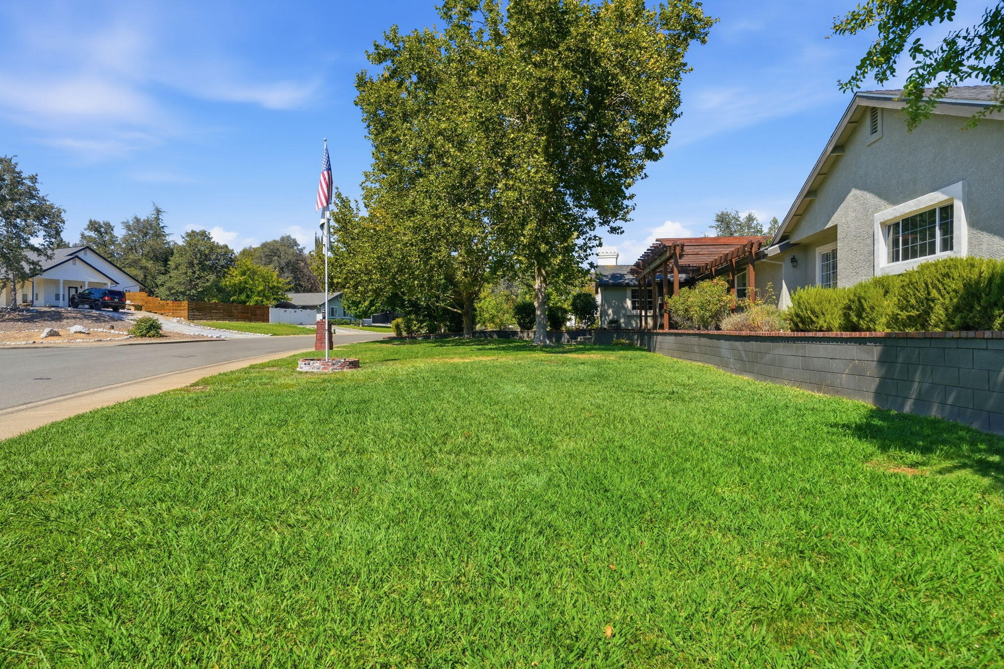 Home exterior with a broad green lawn, mature shade tree, and American flag by the street.