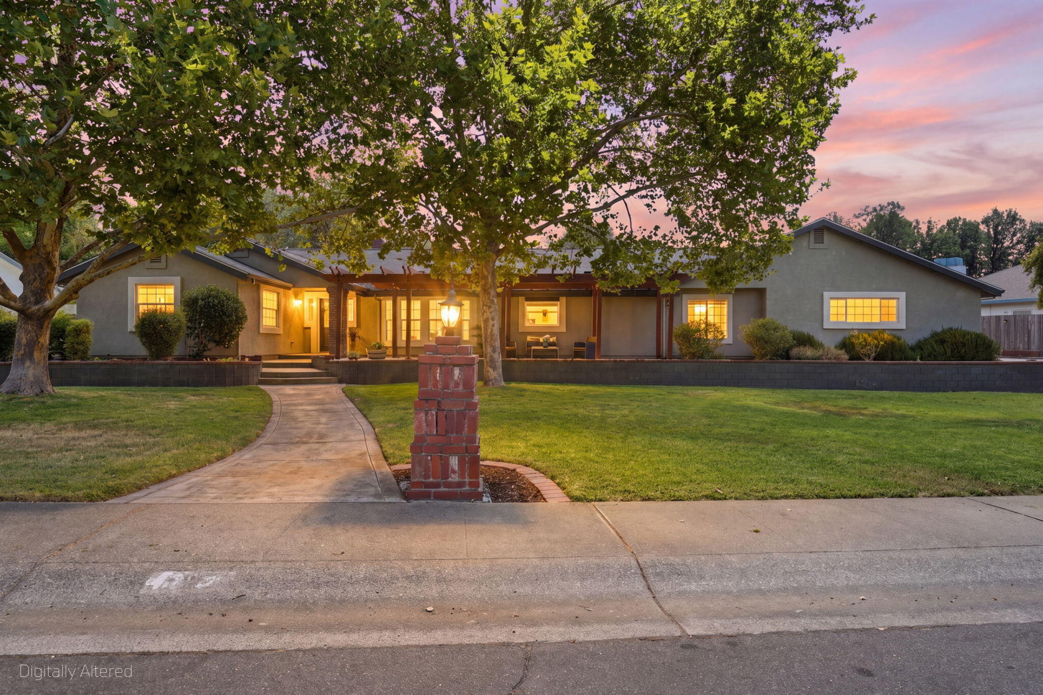 Single-story home with a covered patio, broad lawn, and mature trees at dusk.