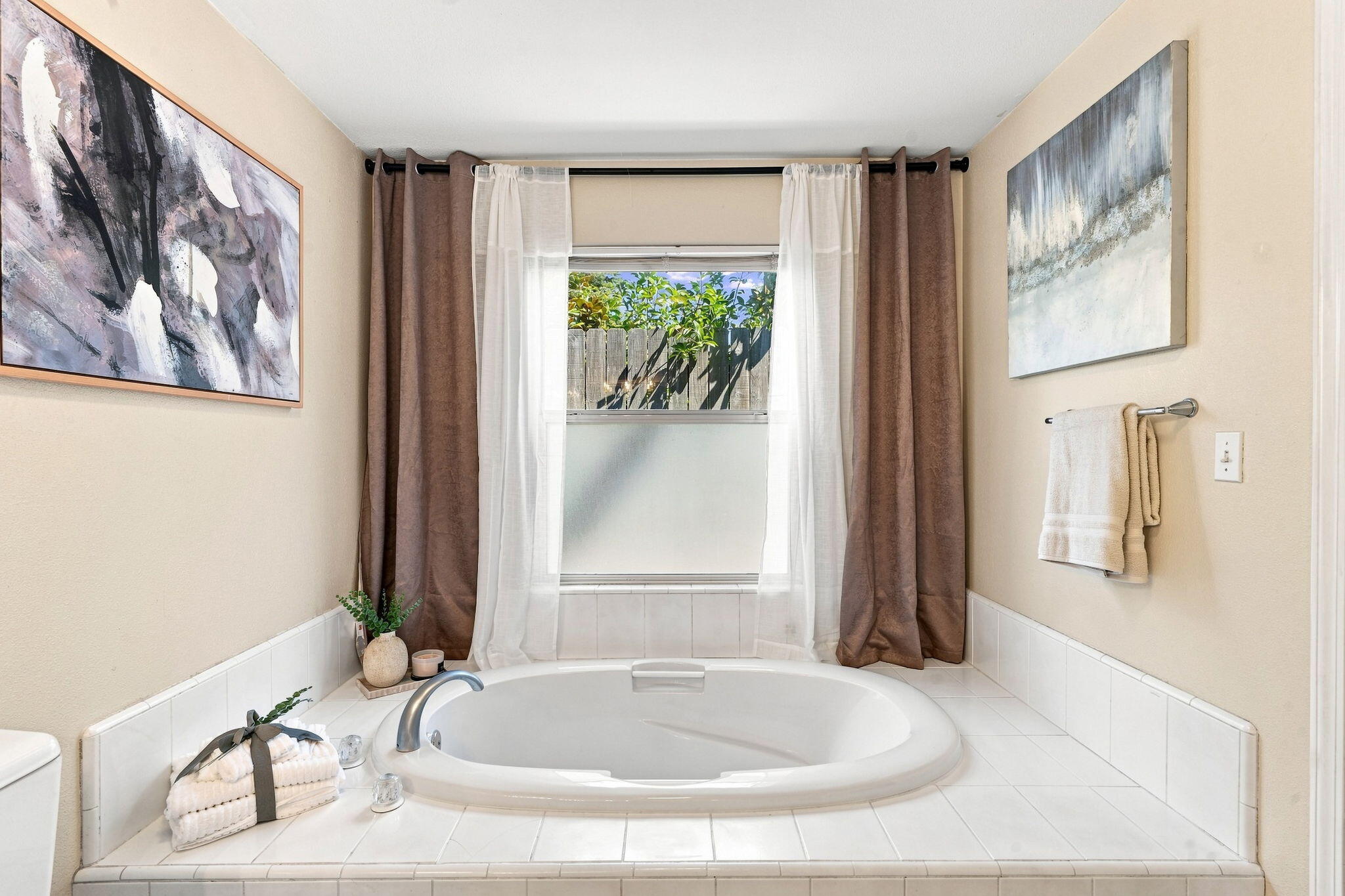 Bathroom with a built-in oval soaking tub, brown curtains, and abstract artwork.