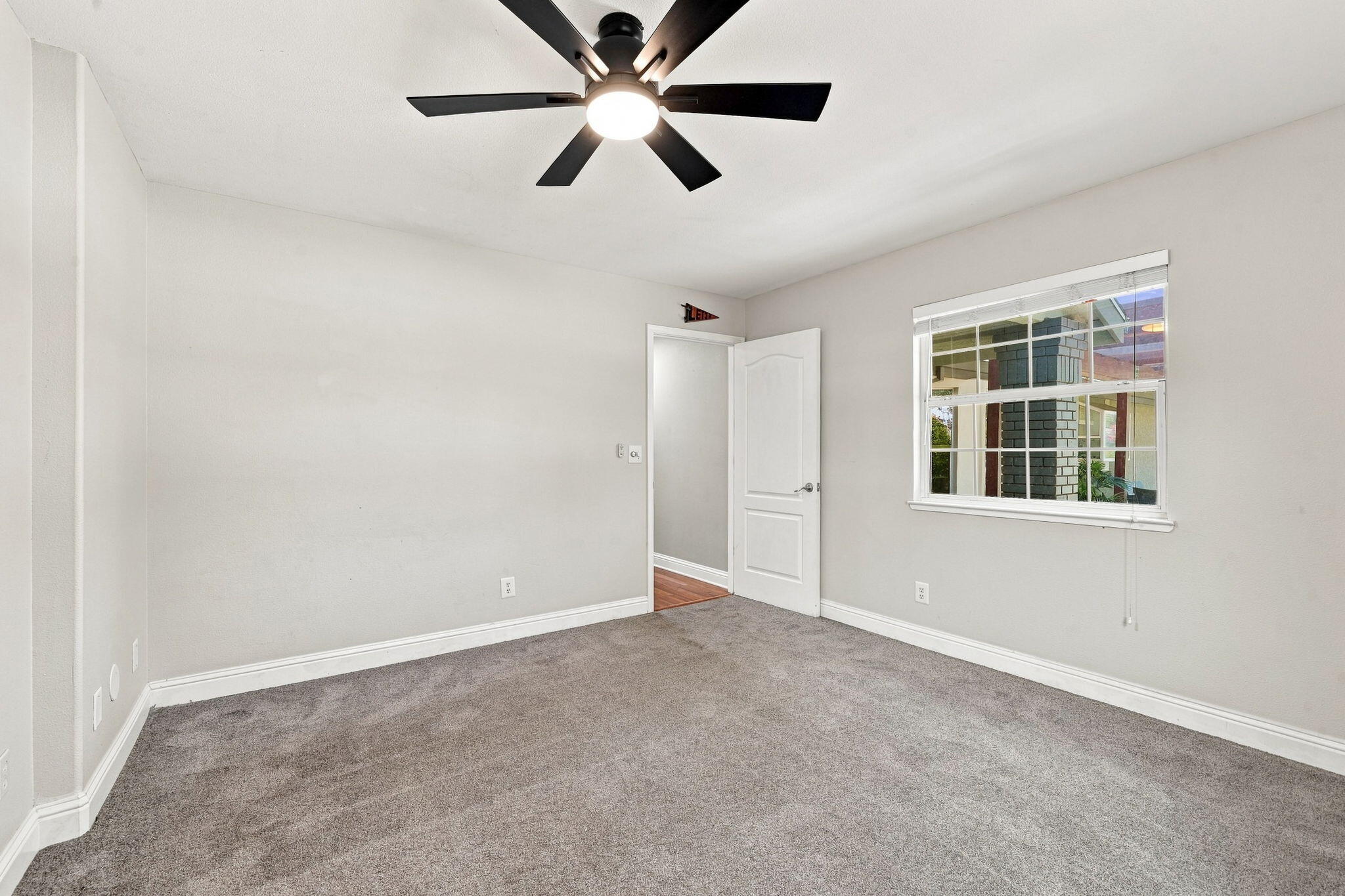 Empty carpeted room with a ceiling fan, window, and open doorway.
