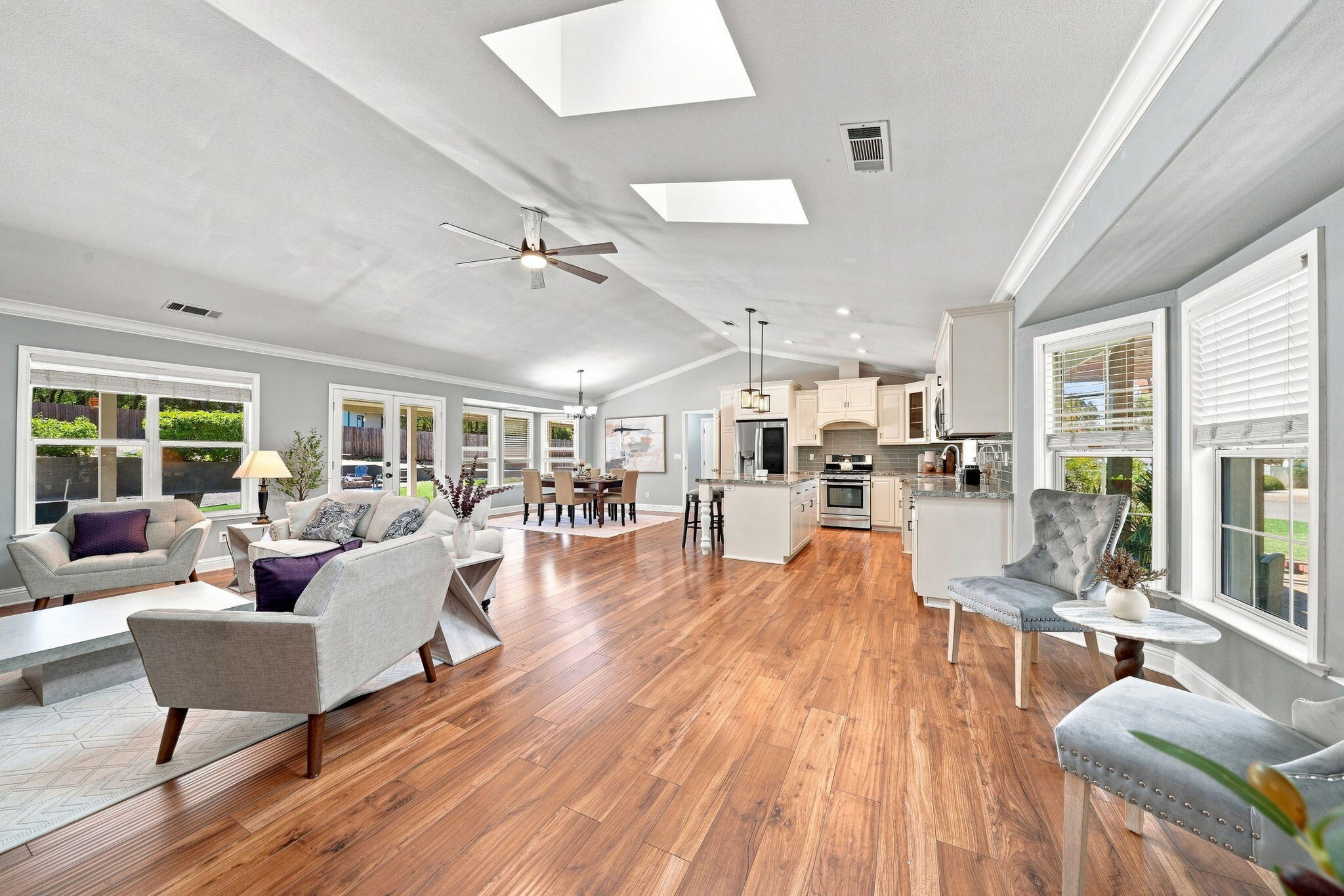 Open-plan living room, dining area, and kitchen with wood floors, skylights, and large windows.