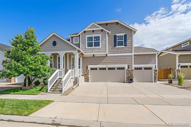 Two-story beige house with a covered porch, three garage doors, and a wide driveway.