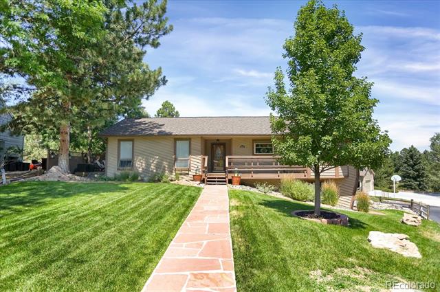 Single-story home with a covered porch and stone walkway through a green lawn, framed by mature trees.