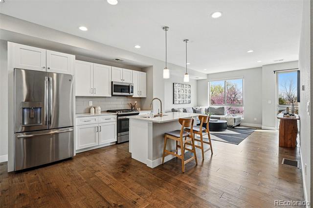 Open-plan kitchen and living area with white cabinets, stainless steel appliances, and a large island.