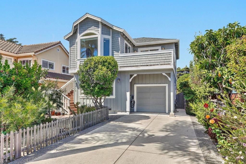 Gray two-story home with a front-facing garage, upper balcony, and landscaped driveway.