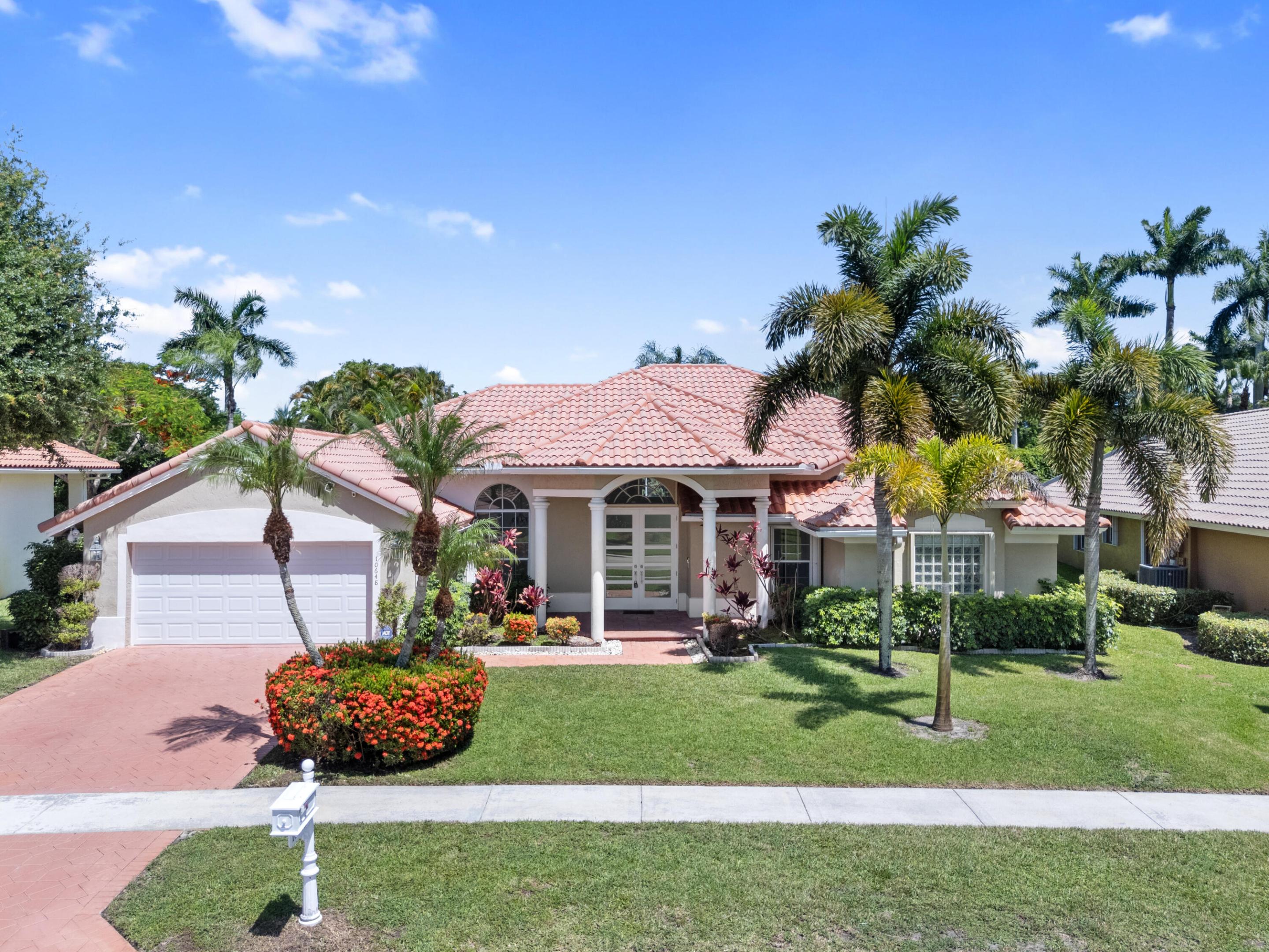 Florida home with a terracotta tile roof, two-car garage, palm trees, and landscaped front yard.