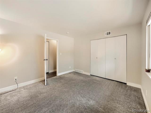 Empty bedroom with gray carpet, a double-door closet, and a window.