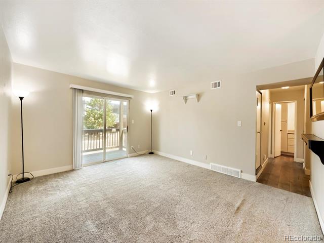 Empty carpeted living room with a sliding glass door opening to a balcony.