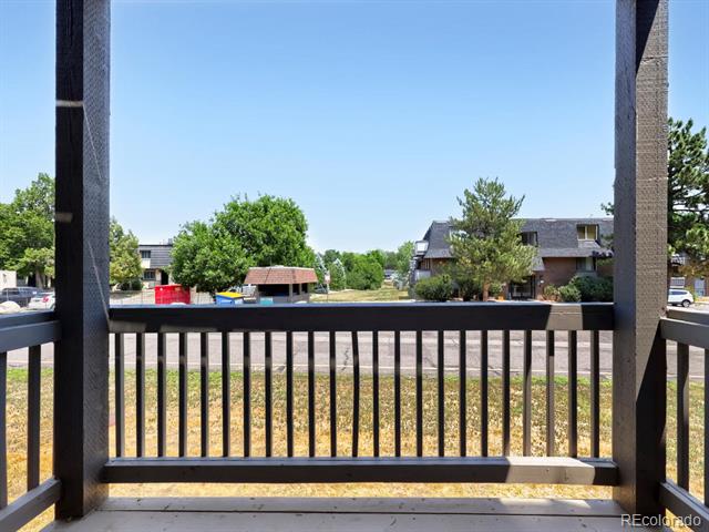 Balcony overlooking trees, a grassy area, and neighboring buildings.