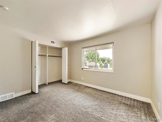Empty bedroom with gray carpet, an open closet, and a window overlooking trees.