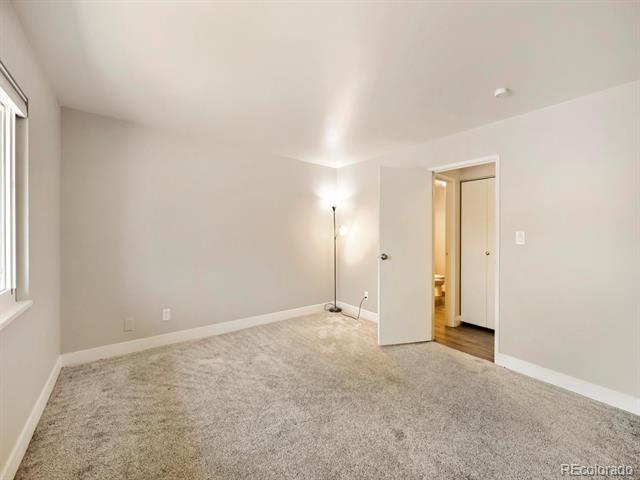Empty carpeted bedroom with neutral walls, a window, and an open door to the hallway.