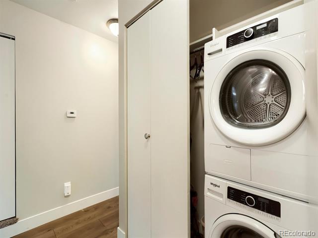 Stacked front-loading washer and dryer in a laundry closet beside a wood-floored hallway.