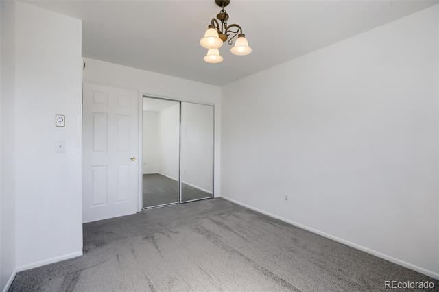 Vacant bedroom with gray carpet, mirrored sliding closet doors, and a multi-light ceiling fixture.