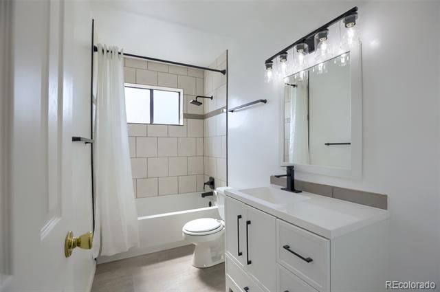Bathroom with a tiled tub and shower, window, toilet, and white vanity with a large mirror.