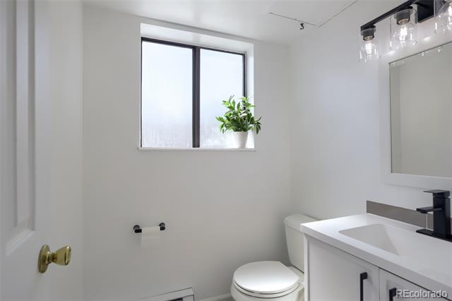 White bathroom with a black faucet, large mirror, and potted plant on the windowsill.