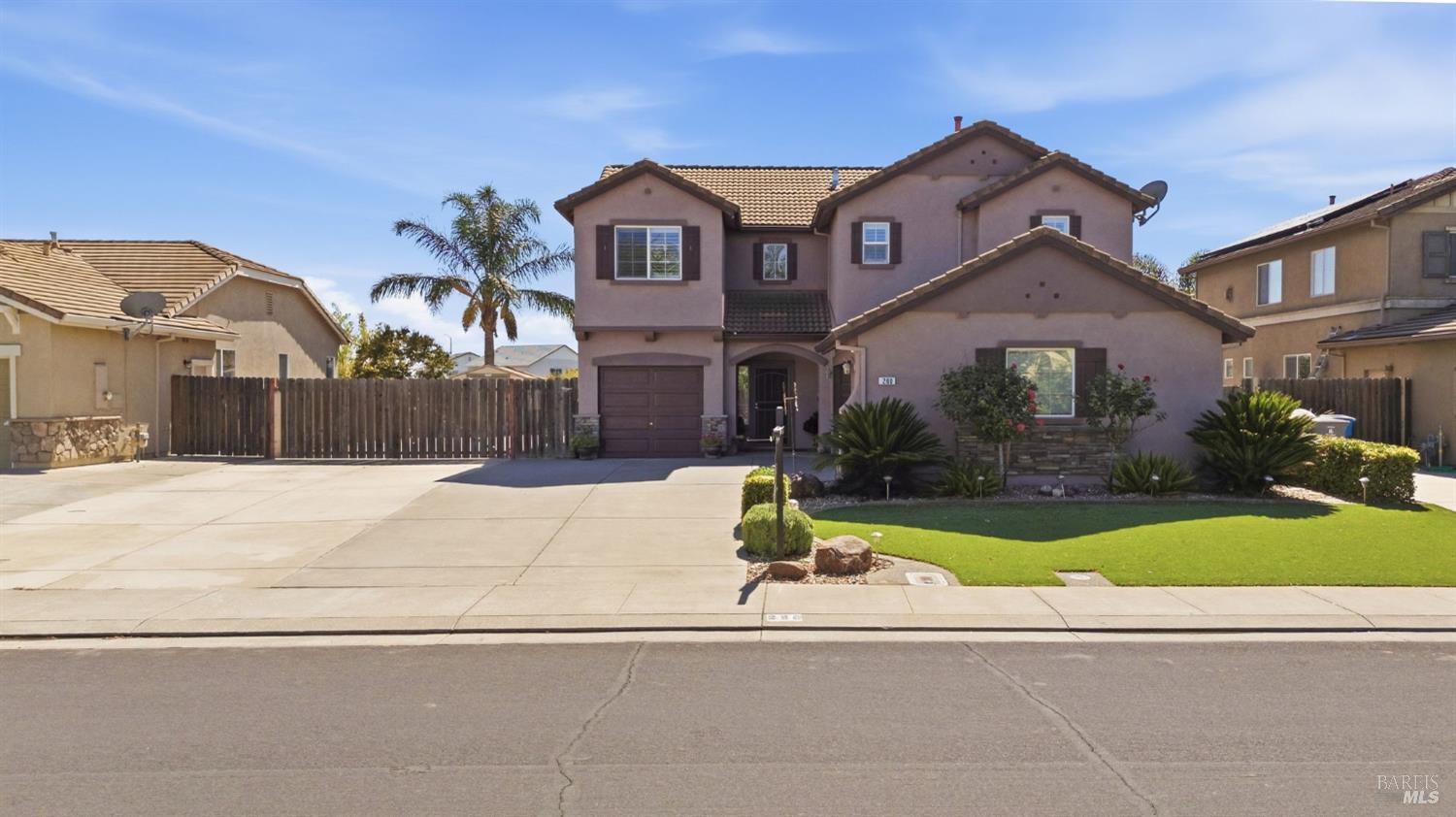 Two-story stucco home with a tiled roof, attached garage, broad driveway, and landscaped front lawn.