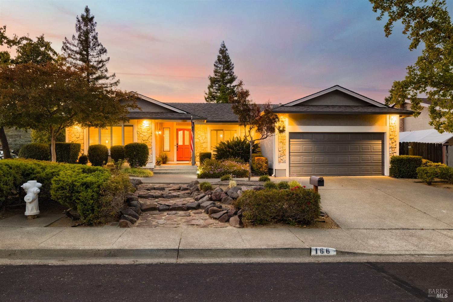 Single-story home with a stone facade, red front door, and attached garage at dusk.