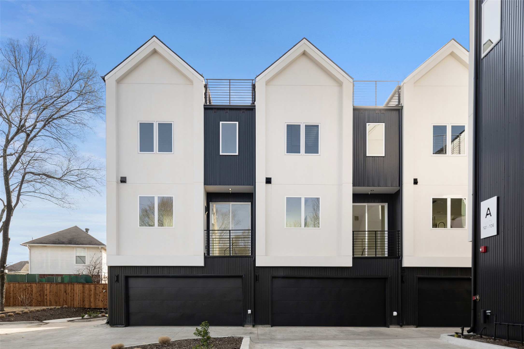 Modern white-and-charcoal townhouse building with gabled facades, balconies, and ground-level garages.