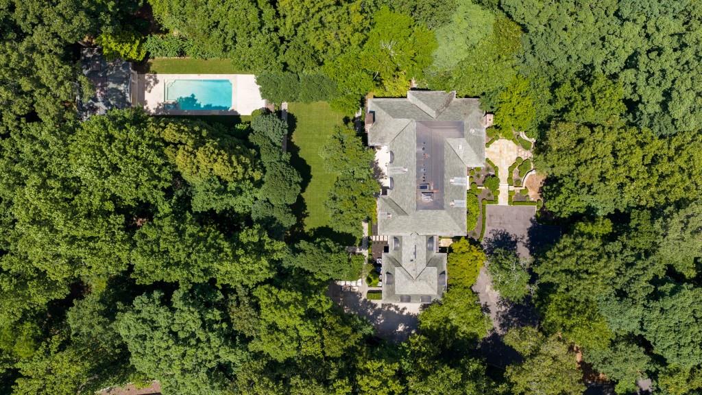 Aerial view of a tree-surrounded home with a swimming pool and landscaped grounds.