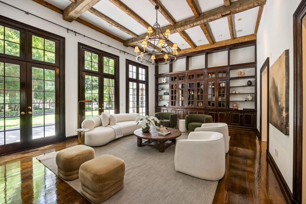 Living room with exposed timber beams, tall windows, and a built-in display cabinet.