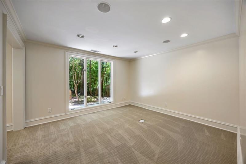 Empty carpeted room with recessed lights and a large window overlooking trees.