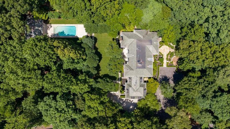 Aerial view of a tree-surrounded home with a swimming pool and landscaped grounds.