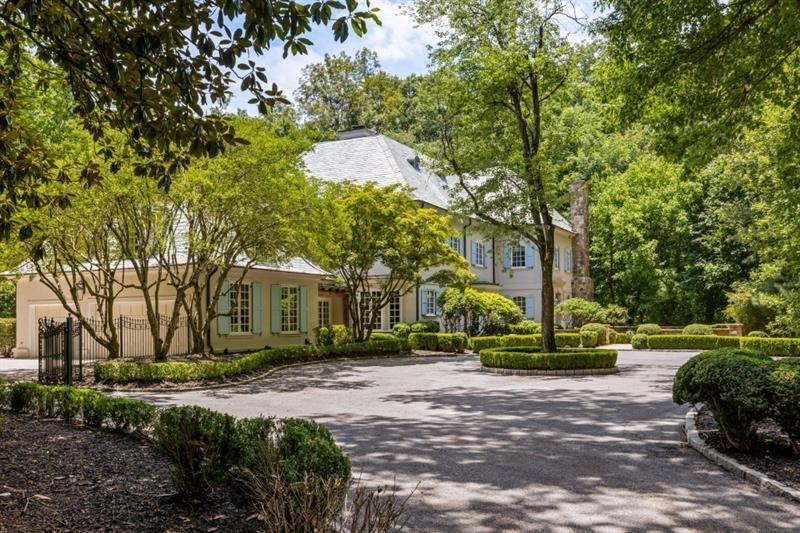 Two-story pale yellow home framed by mature trees, with a curved driveway and landscaped island.