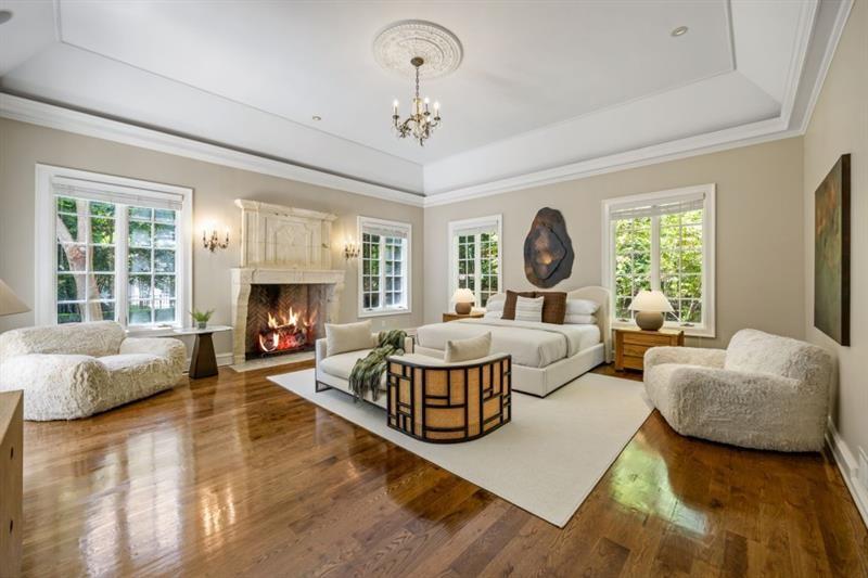 Bedroom with a fireplace, large windows, hardwood floors, and a tray ceiling.