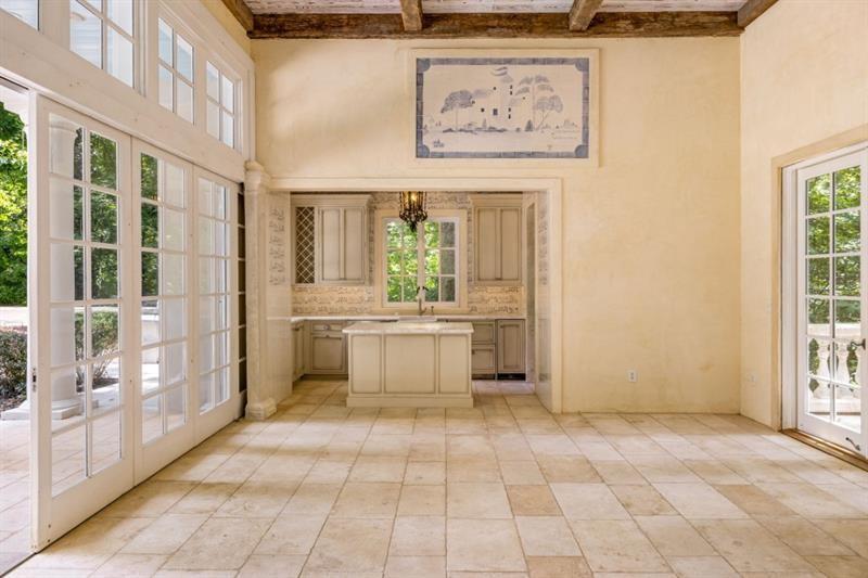 Vacant kitchen and adjoining room with a central island, stone tile floors, French doors, and exposed ceiling beams.
