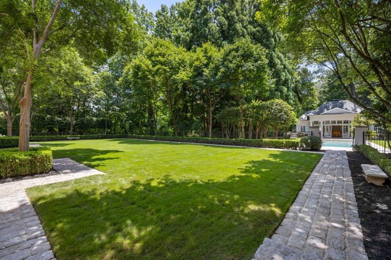 Landscaped backyard with a broad lawn, mature trees, stone paths, and a swimming pool.
