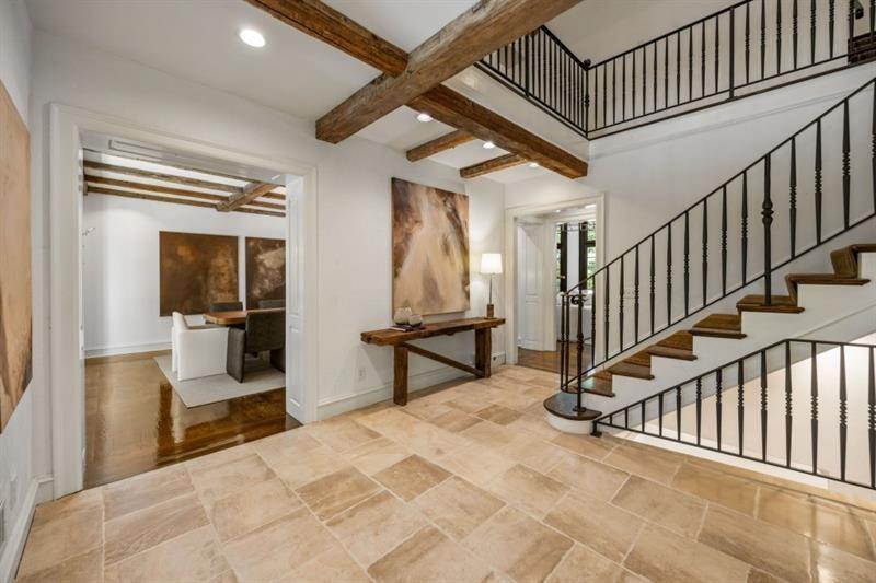 Entry foyer with exposed wood beams, stone tile, and a black iron-railed staircase.