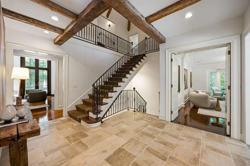 Foyer with a sweeping staircase, exposed timber beams, and light stone tile flooring.
