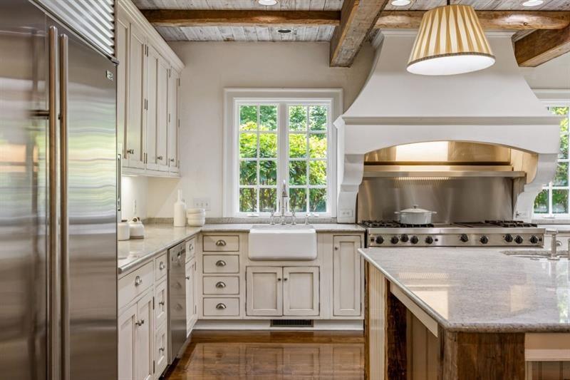 Kitchen with a farmhouse sink, stainless range, marble counters, and exposed wood ceiling beams.