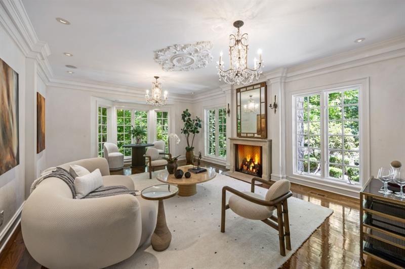 Living room with a lit fireplace, crystal chandeliers, and large windows.