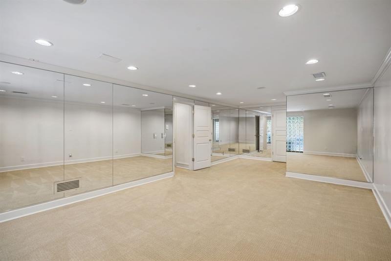 Empty carpeted room with mirrored walls and recessed lighting.