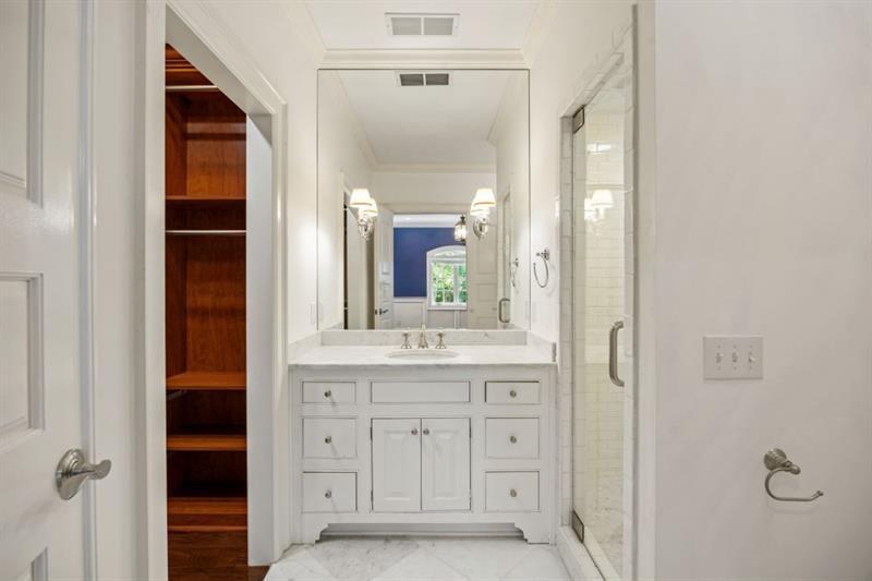 Bathroom with a white paneled vanity, glass shower, marble surfaces, and open wood shelving.