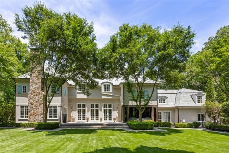 Large two-story house with a stone chimney, mature trees, and a manicured front lawn.