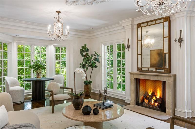 Living room with a lit fireplace, crystal chandeliers, and tall divided-light windows.