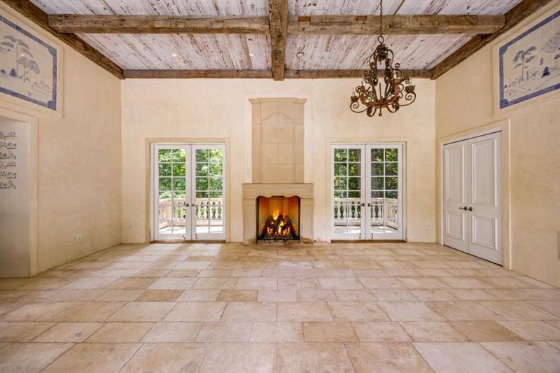 Empty living room with a lit fireplace, French doors, and exposed wood ceiling beams.