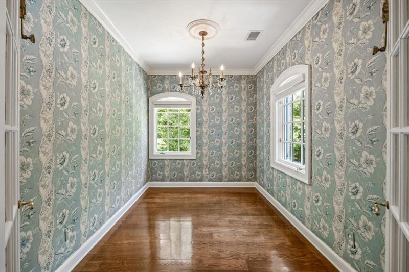 Empty room with floral wallpaper, polished hardwood floors, chandelier, and two windows.