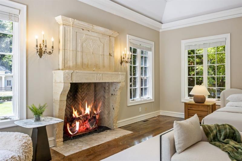 Living room with a carved stone fireplace, burning fire, tall windows, and a light sofa.