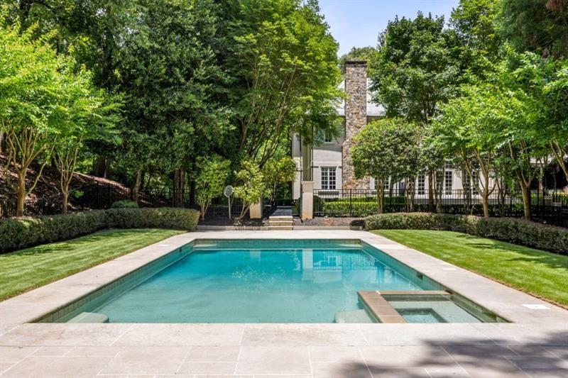 Backyard swimming pool and raised spa framed by mature trees, with the house and stone chimney behind.