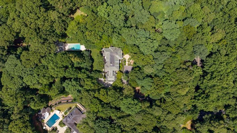 Aerial view of a house surrounded by dense trees, with nearby swimming pools.