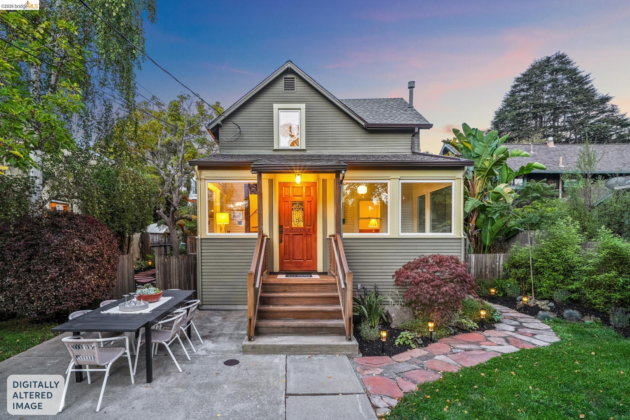 Gray two-story house with a warmly lit orange front door, landscaped stone path, and patio at dusk.